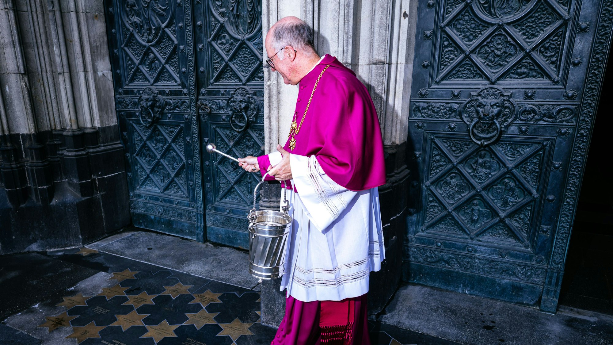 Weihwasser wird auf Sterne am Boden gesprenkelt.