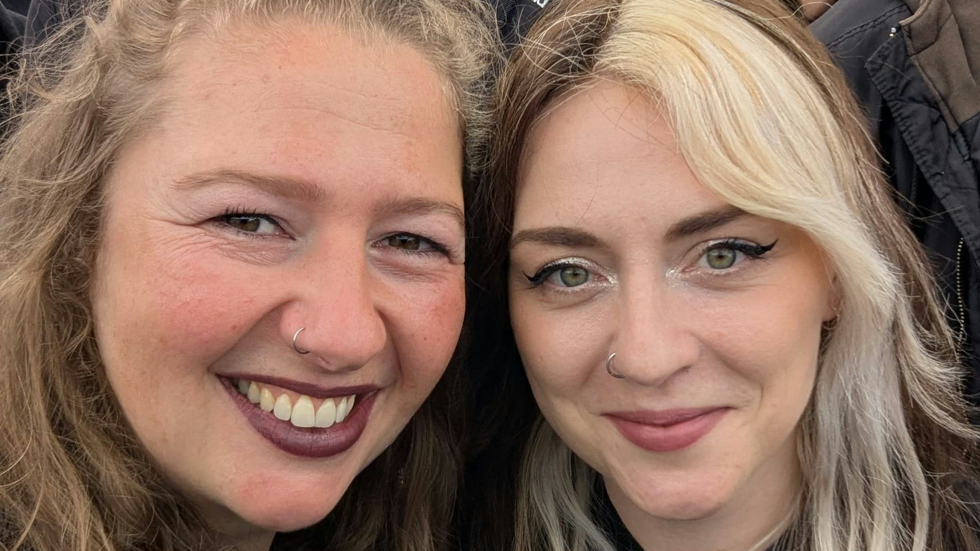 Zwei Frauenlachen in Schwarz gekleidet in die Kamera.