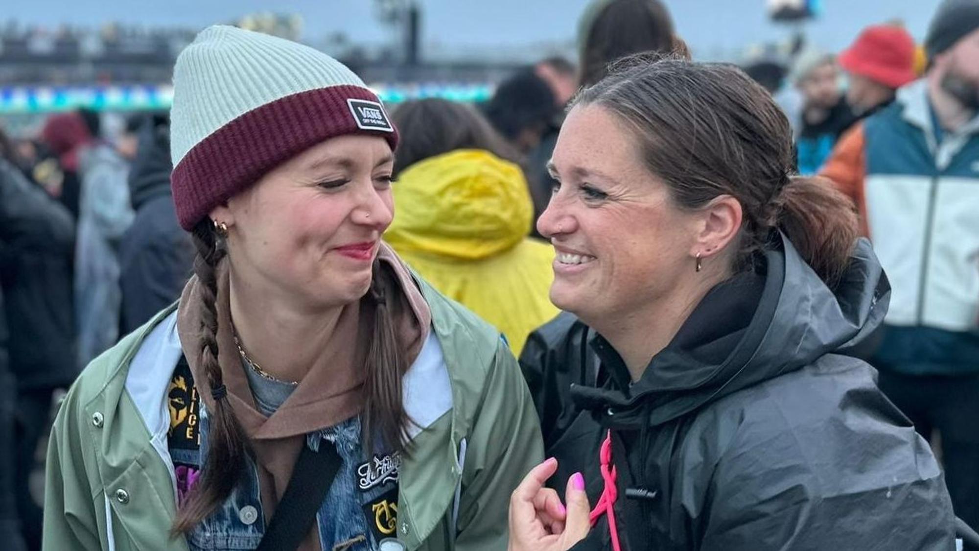 Zwei Frauen in Regenjacken schaue sich an und lachen.