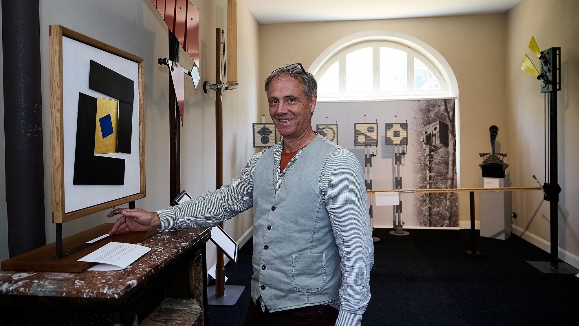Ein Mann in Hemd und Weste steht in einer Ausstellung.