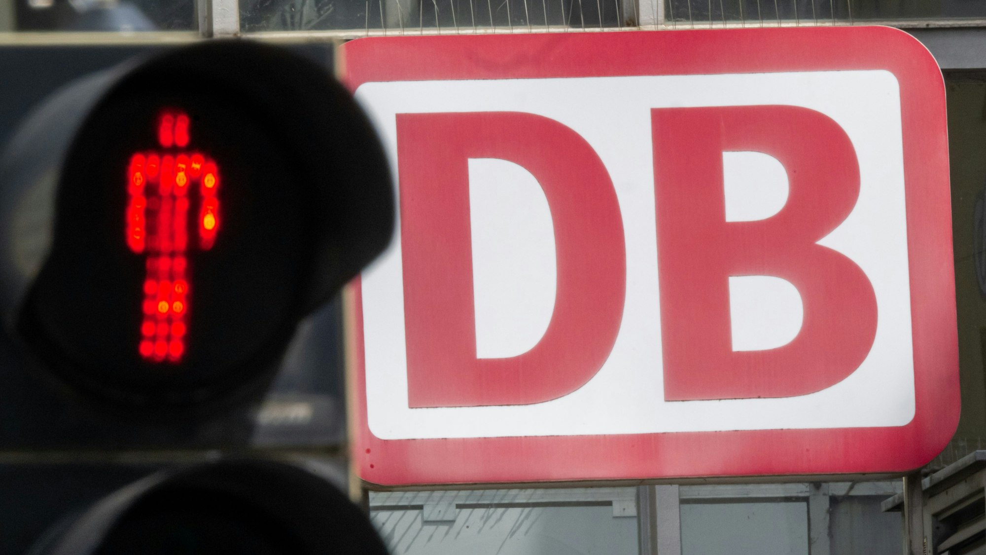 Eine Fußgängerampel, vor dem Logo der Deutschen Bahn (DB) am Münchner Hauptbahnhof, leuchtet Rot. (Archivbild)