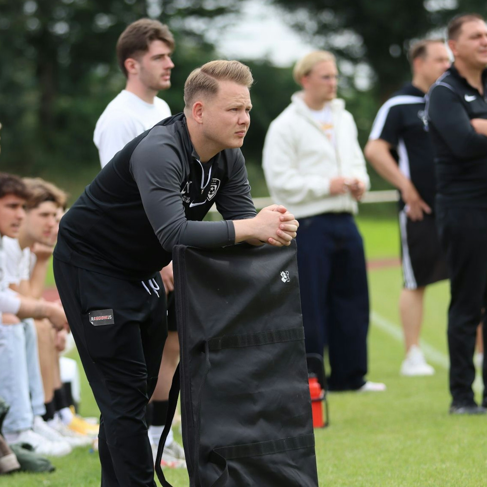 Christopher Kockerols lehnt auf eine noch eingepackte Taktiktafel am Spielfeldrand und schaut grimmig.