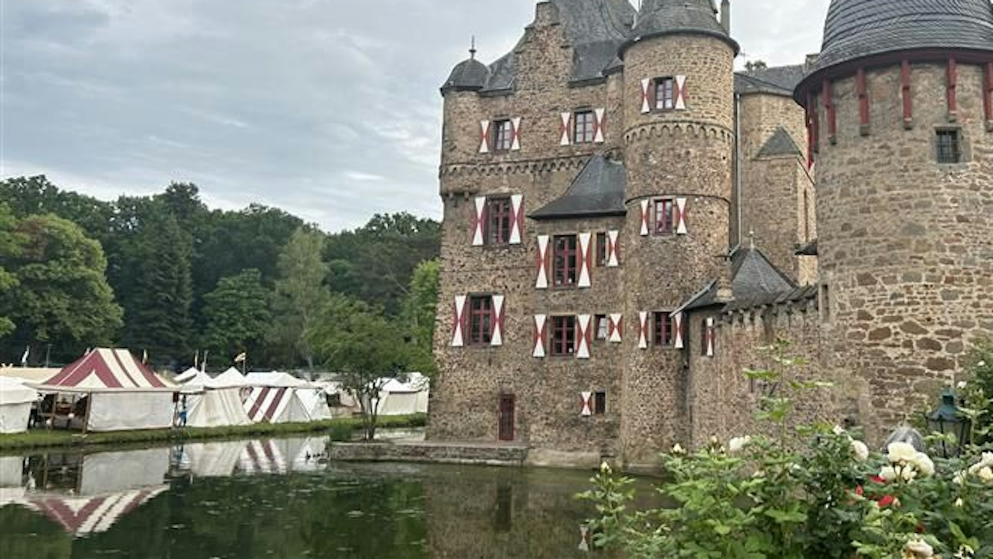 Die Burg Satzvey und die mittelalterlichen Festzelte spiegelt sich im Wasser des Burggrabens.