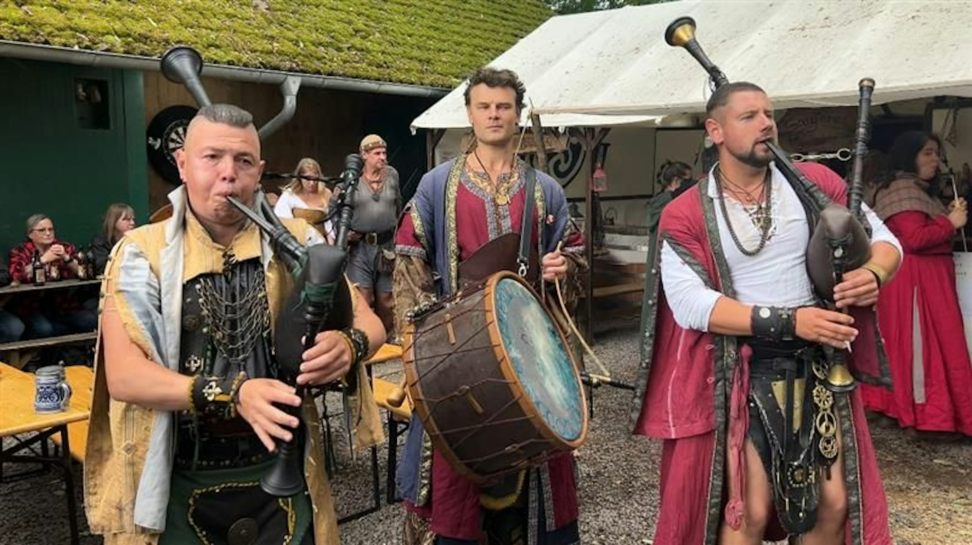 Drei Männer in mittelalterlicher Kleidung musizieren mit Dudelsack und Trommel.