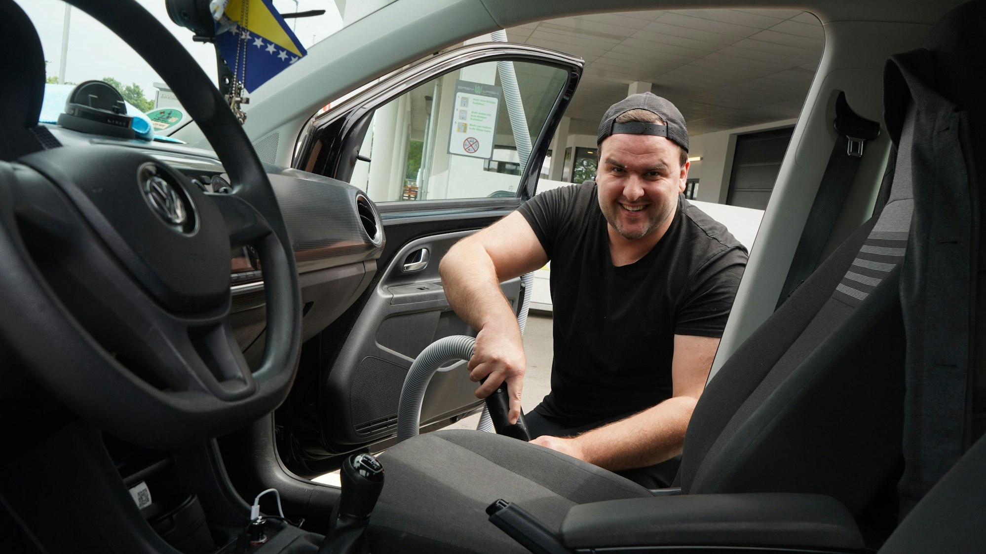 Das Foto zeigt einen Mann, der den Innenraum seines Autos saugt.