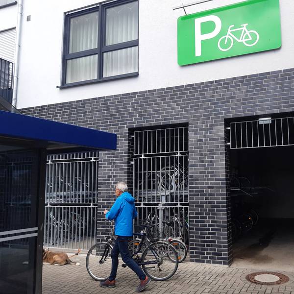 Das Foto zeigt einen Mann, der ein Rad vor einer Fahrradgarage schiebt.