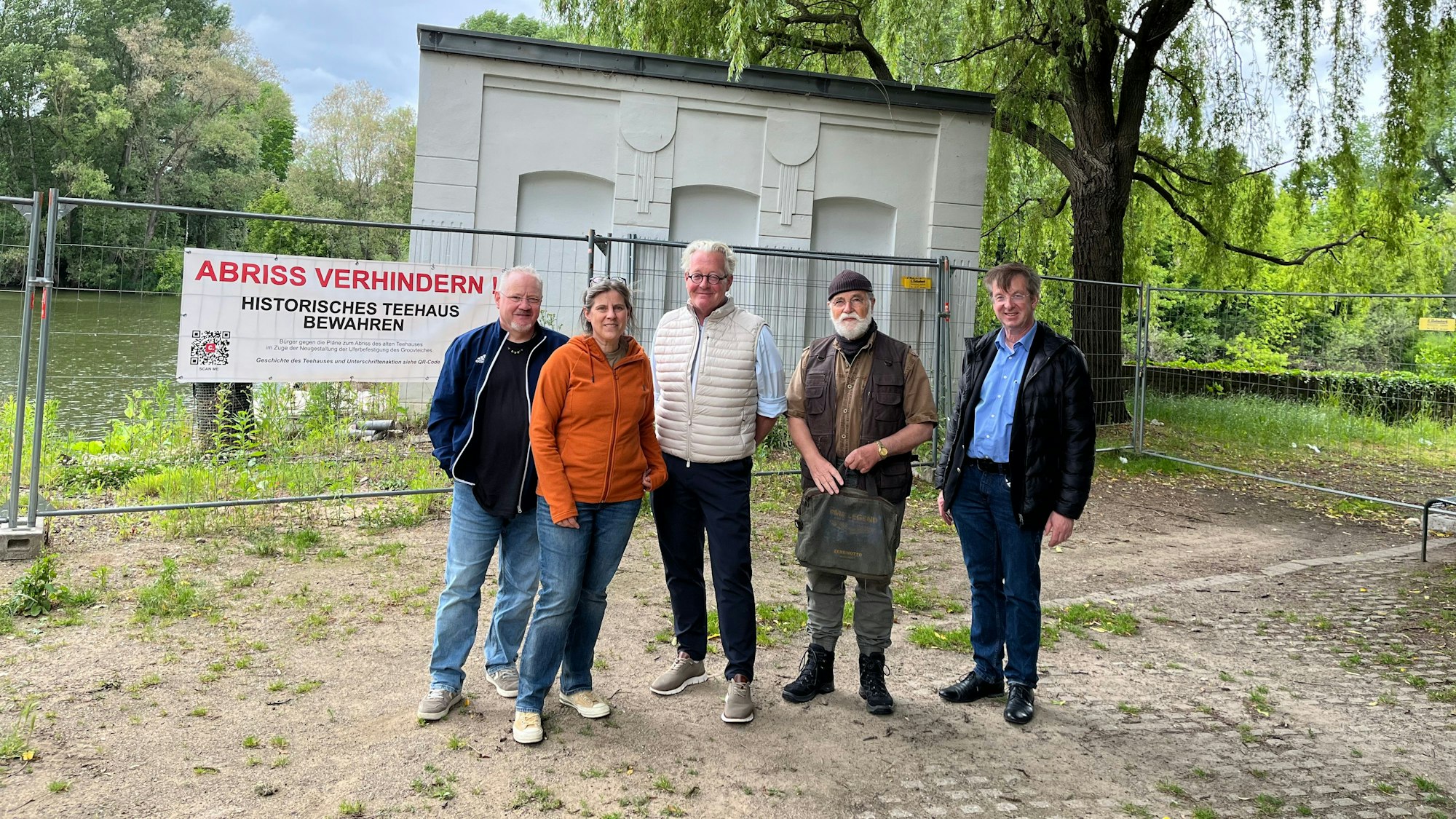 Vier Männer und eine Frau stehen vor einem kompakten alten Gebäude, das von einem Bauzaun abgesperrt ist.