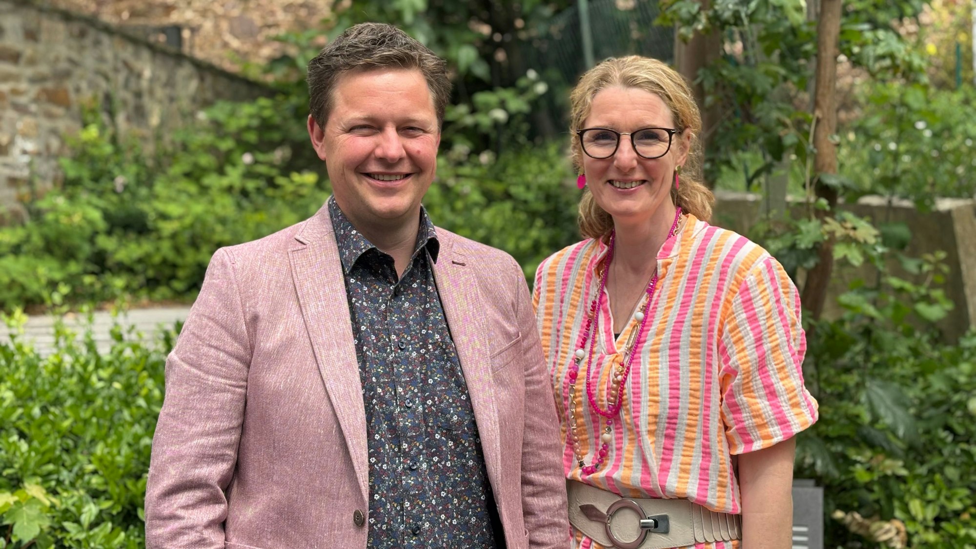 Christian Meyer trägt ein Sakko und ein gemustertes Hemd. Neben ihm steht Claudia Rapp-Ludwig in einer sommerlichen Bluse, mit einer breiten Schnalle und Ketten. Sie stehen im Grünen.
