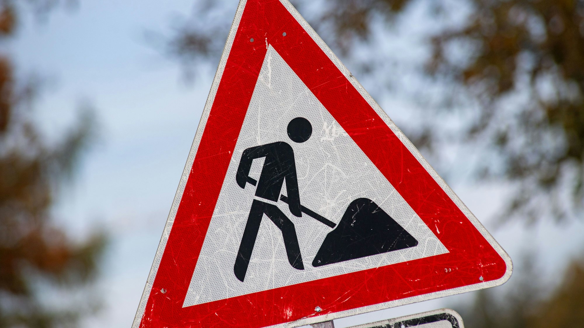 Ein zerkratztes Schild mit dem Piktogramm eines Bauarbeiters zur Beschilderung einer Baustelle.