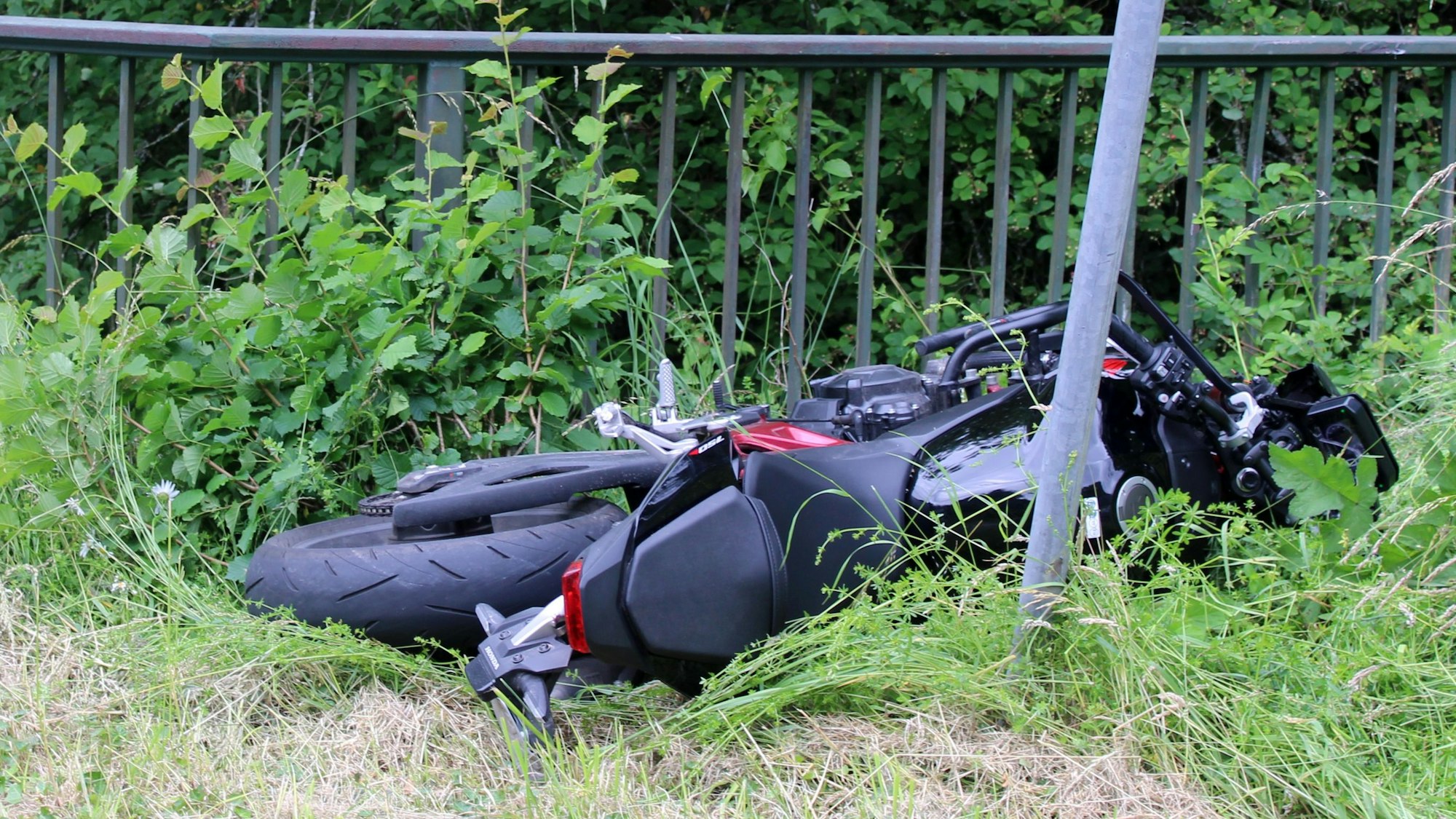 Ein verunfalltes Motorrad (Honda) liegt in einer Wiese neben einem Geländer in Odenthal-Altenberg.