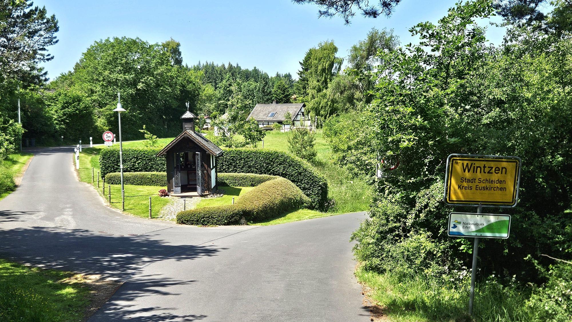 Blick auf den Ortseingang aus Richtung Broich mit der kleinen Kapelle und dem Ortsschild.