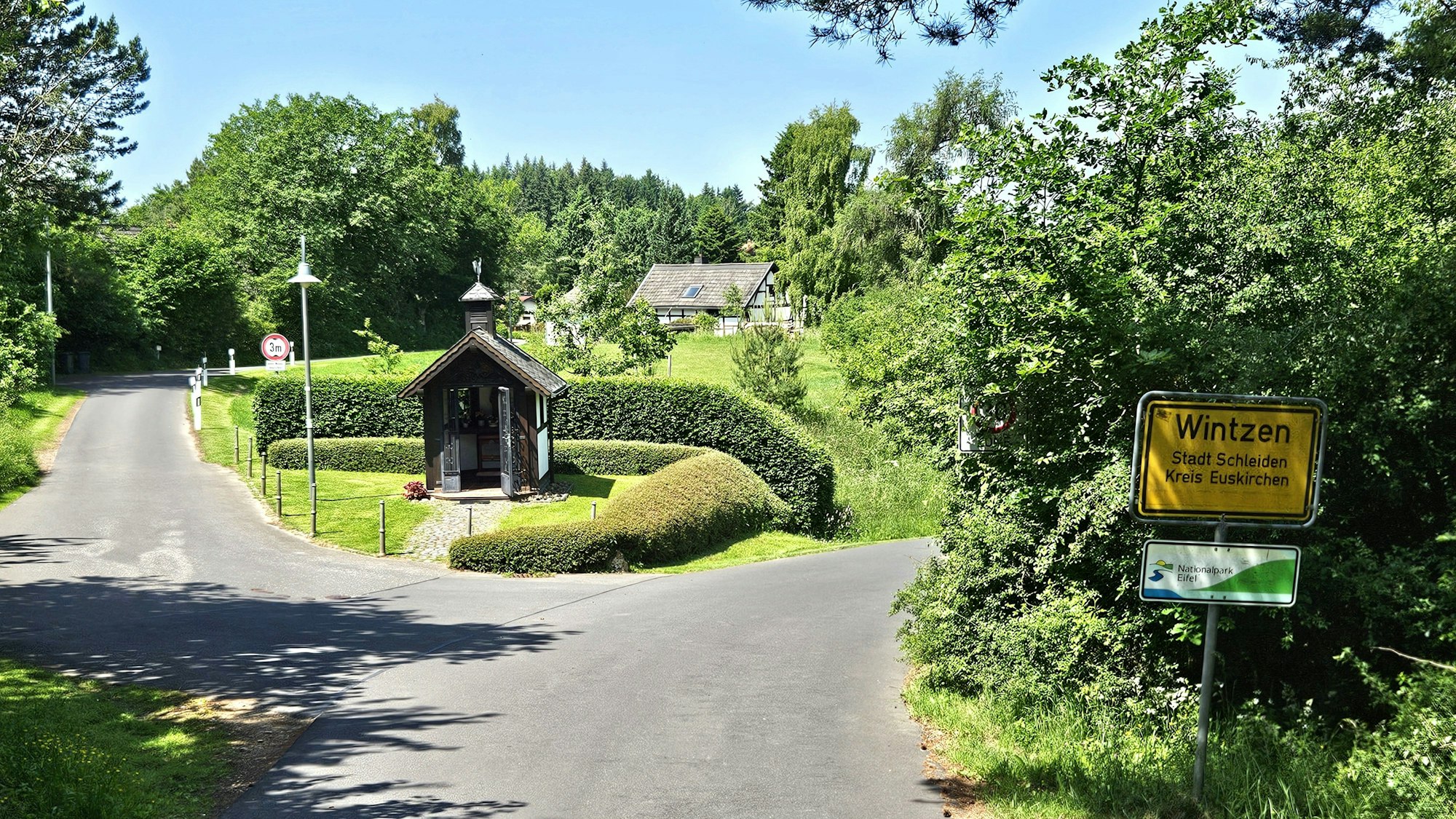 Blick auf den Ortseingang aus Richtung Broich mit der kleinen Kapelle und dem Ortsschild.