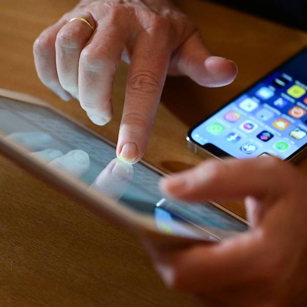 Eine Person tippt auf ein iPad, vor ihr liegt ein Smartphone auf dem Tisch