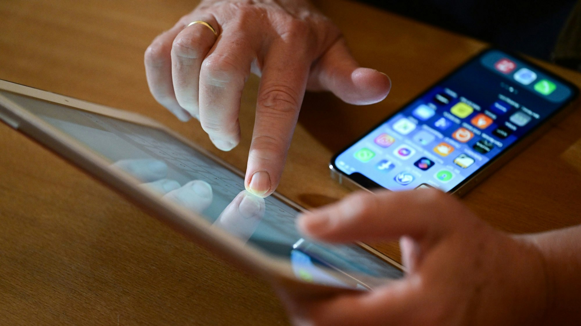 Eine Person tippt auf ein iPad, vor ihr liegt ein Smartphone auf dem Tisch