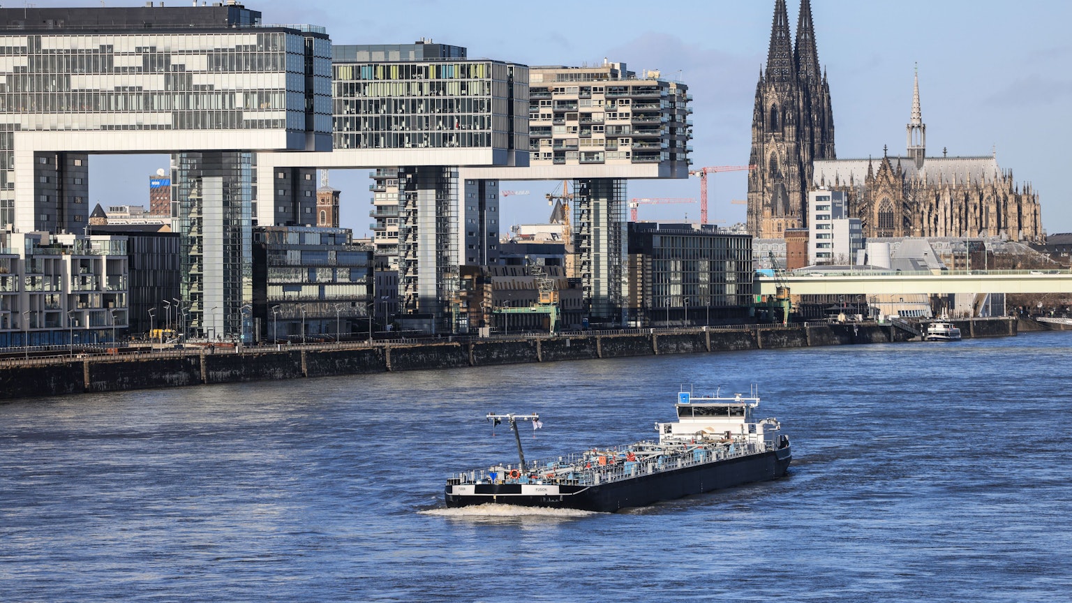 Köln: Ein Binnenschiff fährt bei Sonnenschein an den Kranhäusern (l) und dem Dom (r) vorbei über den Rhein.