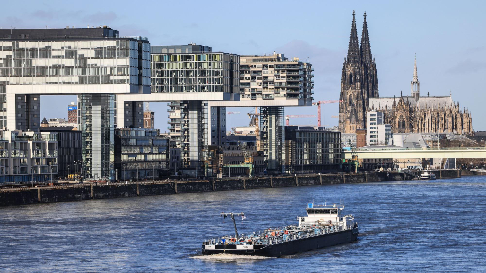 Köln: Ein Binnenschiff fährt bei Sonnenschein an den Kranhäusern (l) und dem Dom (r) vorbei über den Rhein.