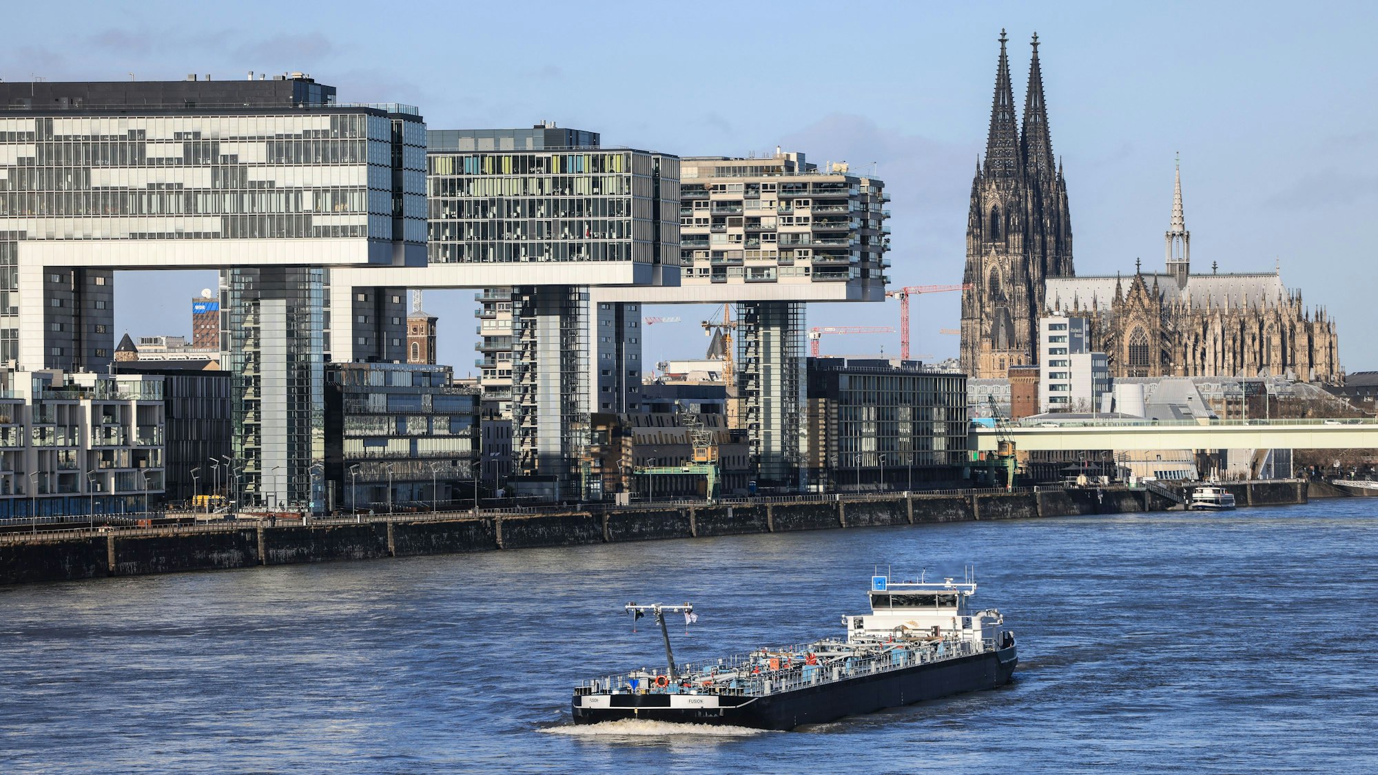 Köln: Ein Binnenschiff fährt bei Sonnenschein an den Kranhäusern (l) und dem Dom (r) vorbei über den Rhein.
