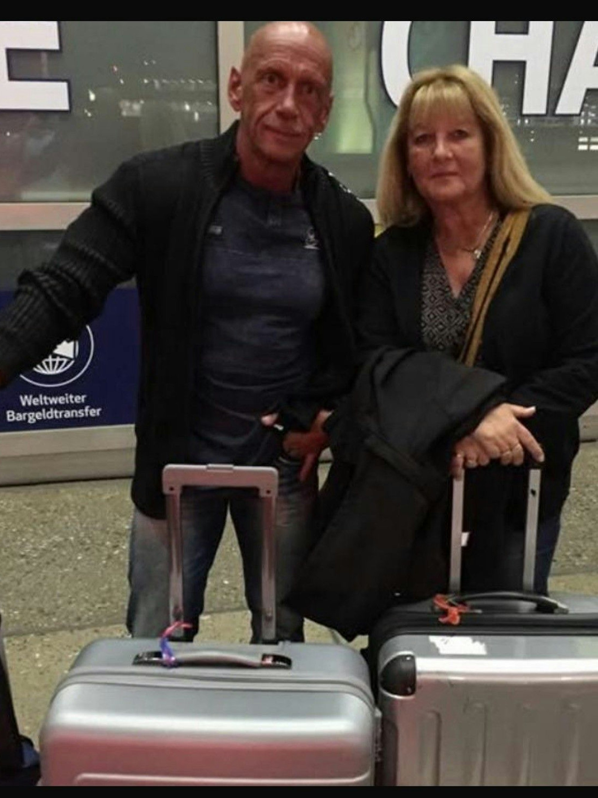 Auf dem Bild ist das Ehepaar mit Koffern am Flughafen zu sehen.