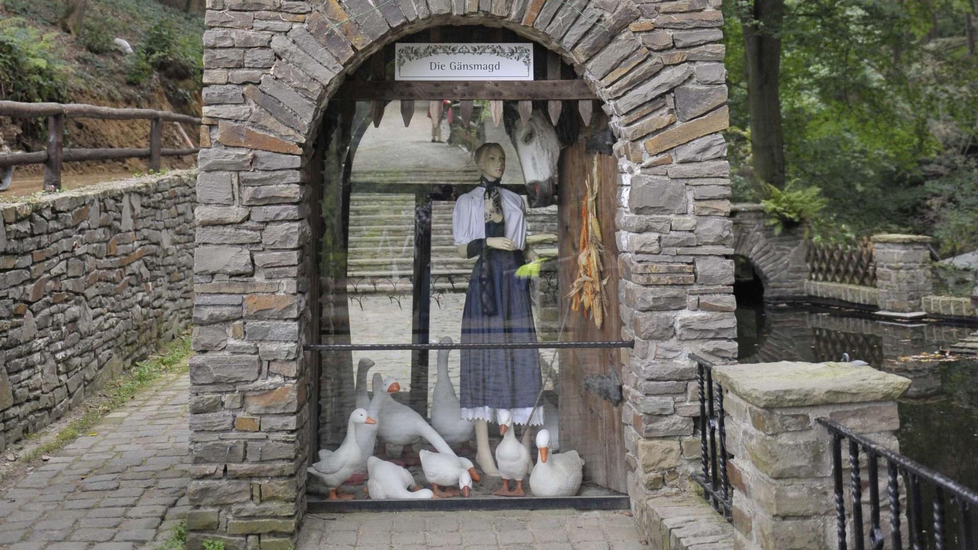 In einem Bruchsteinbogen steht hinter Glas eine Figur mit Gänsen.