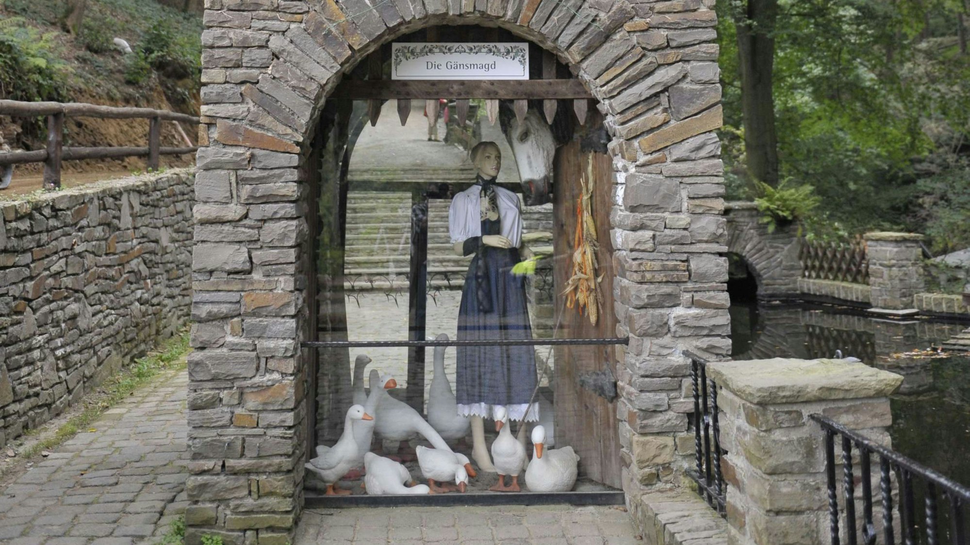 In einem Bruchsteinbogen steht hinter Glas eine Figur mit Gänsen.