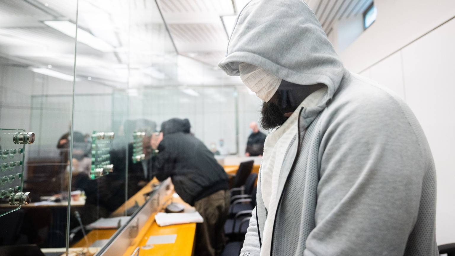 Abu Walaa (vorn), mutmaßlicher Anführer der Terrormiliz Islamischer Staat (IS) in Deutschland, steht im Oberlandesgericht hinter einer Glasscheibe. Foto: Julian Stratenschulte/dpa Pool/dpa