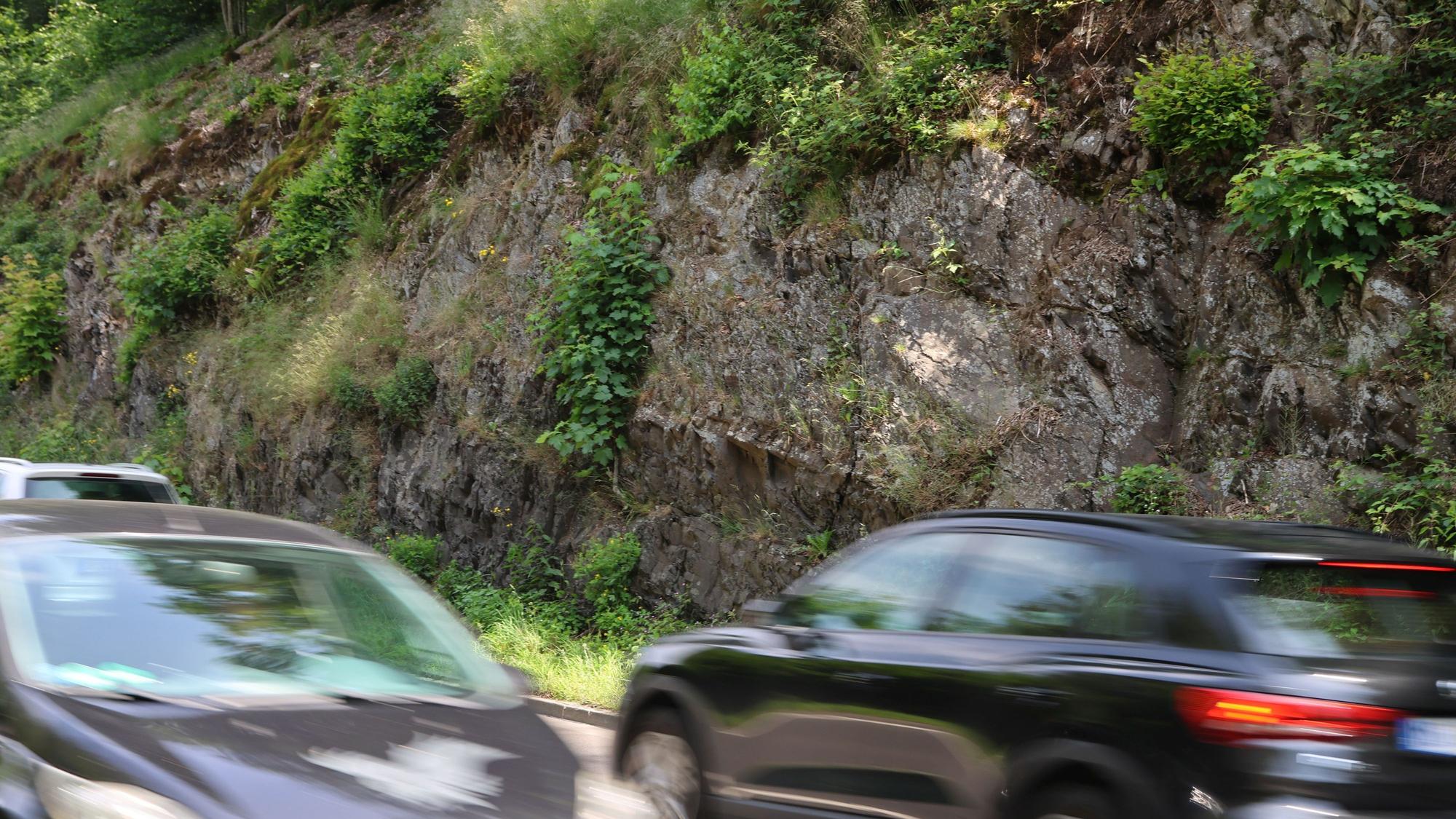 Eine Felswand, davor vorbeifahrende Autos.