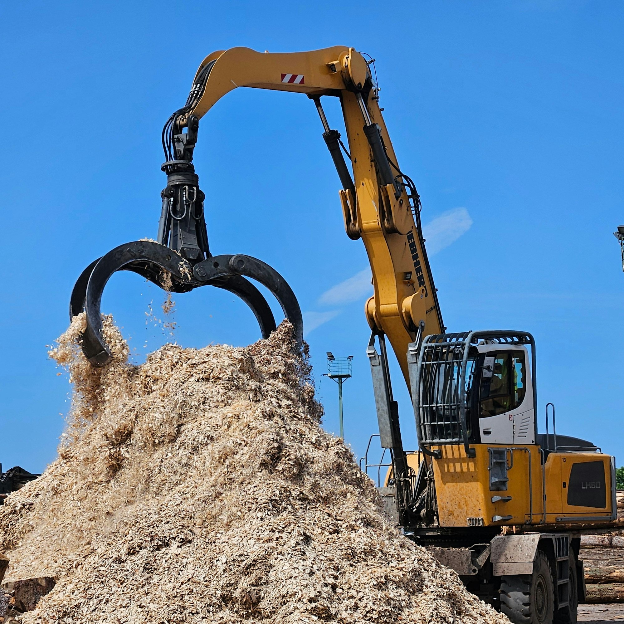 Ein Bagger schichtet die Holzspäne mit seinem Greifer zu einem Haufen auf.