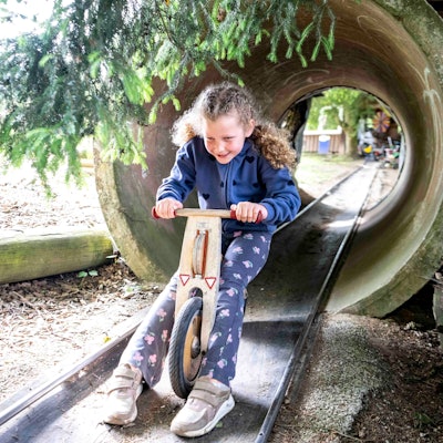 Das Bild zeigt ein Mädchen, das mit einem Laufrad durch ein Rohr fährt.