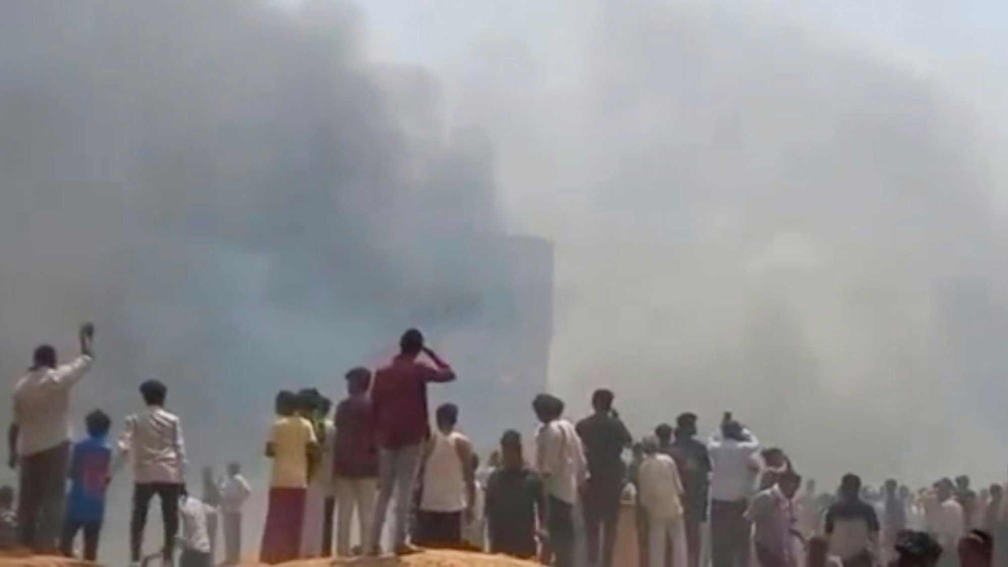 12.06.2025, Indien, Ahmedabad: *** VIDEOGRAB *** Menschen sehen Rauch aufsteigen, nachdem ein Flugzeug in Ahmedabad im indischen Bundesstaat Gujarat abgestürzt ist. Foto: Mohan Nakum/Mohan Nakum/AP/dpa - ACHTUNG: Nur zur redaktionellen Verwendung im Zusammenhang mit der aktuellen Berichterstattung und nur mit vollständiger Nennung des vorstehenden Credits +++ dpa-Bildfunk +++