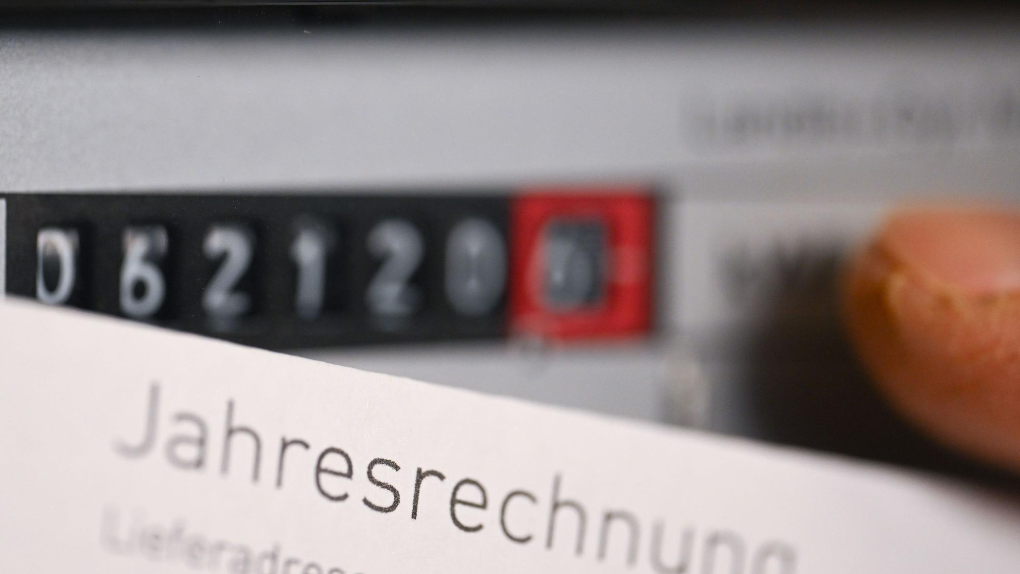 Eine Jahresrechnung für Strom wird vor einen Stromzähler in einem Privathaushalt gehalten.