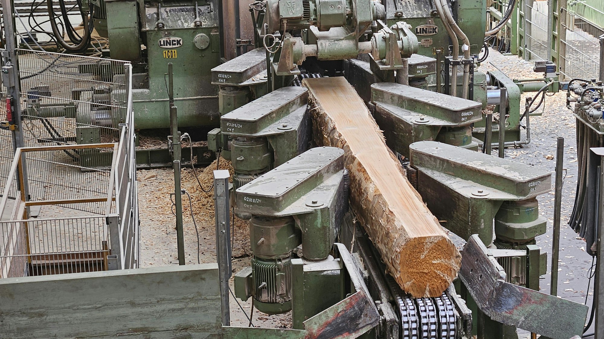 Blick auf eine Maschine mit einem Stamm, an dem an einer Seite die Rinde bereits abgeschnitten wurde.