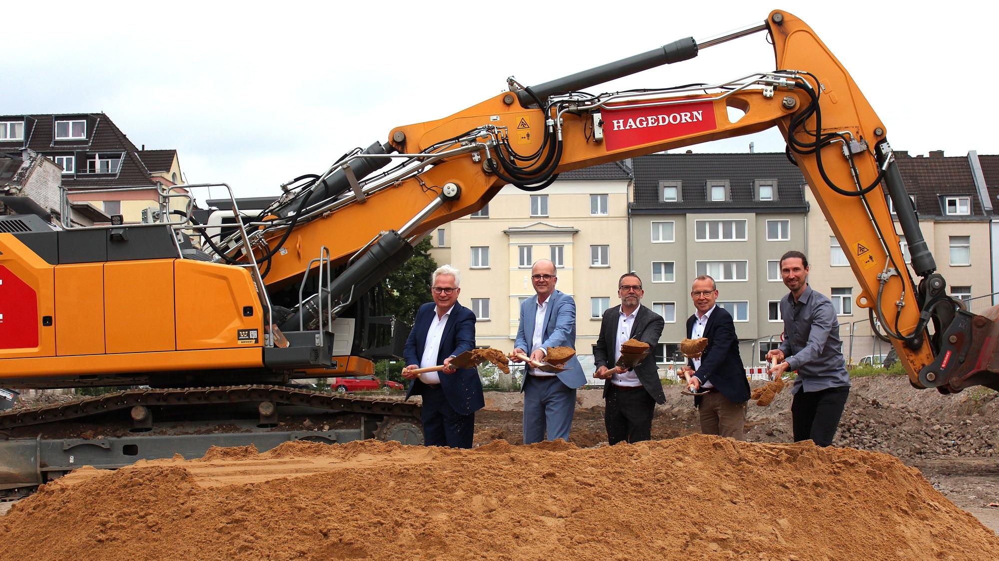 Moderne-Stadt-Geschäftsführer Andreas Röhrig, Baudezernent Markus Greitemann, Wohnungsgenossenschafts-Vorstand Christoph Moossen, Genossenschafts-Abteilungsleiter Neubau und Modernisierung Rainer Burkhardt sowie Architekt Tim Dückers (v.l.) beim gemeinsamen Spatenstich unter dem Bagger-Greifarm.