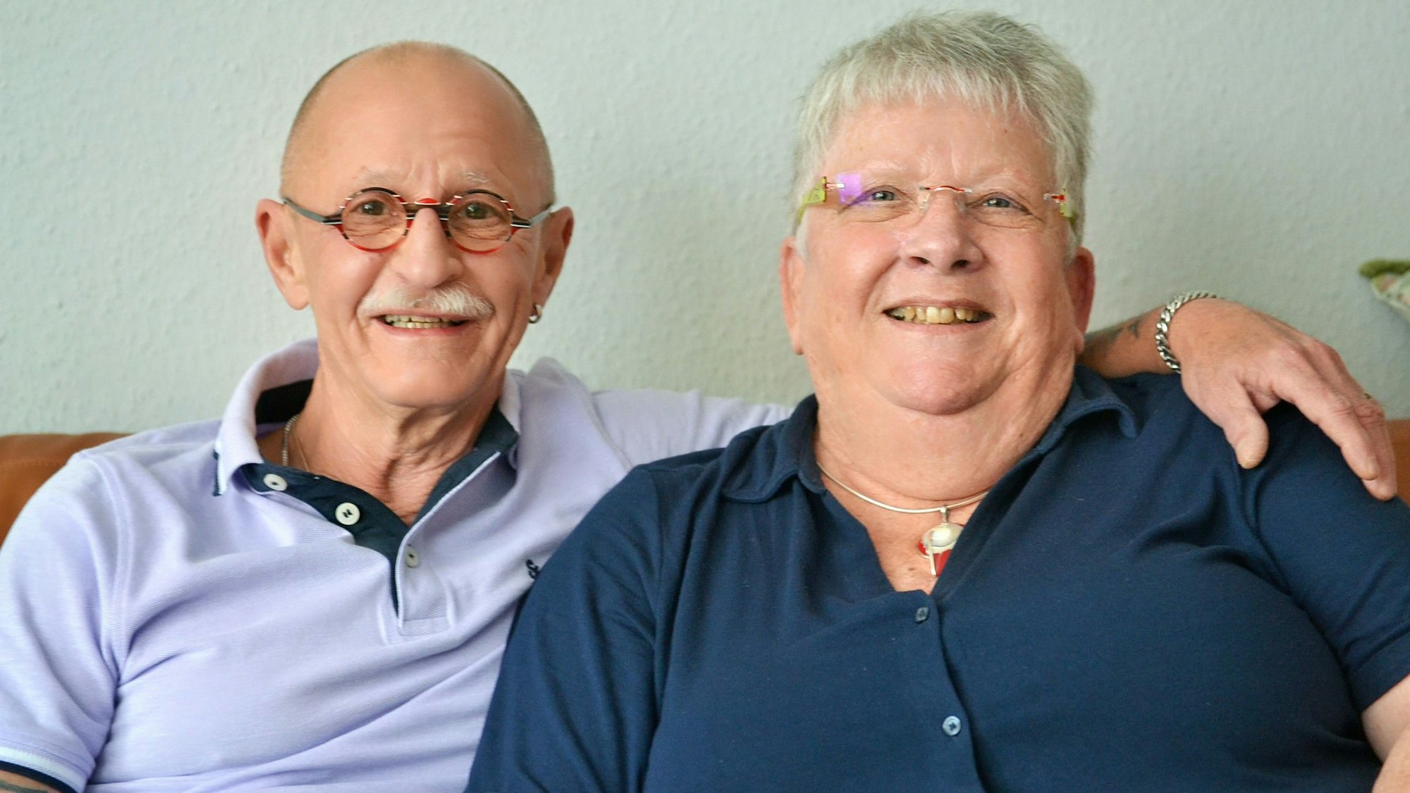 Angelika und Heinz Dieter Bolz sitzen auf einer Couch. Er hält seinen Arm um sie. Beide lächeln.