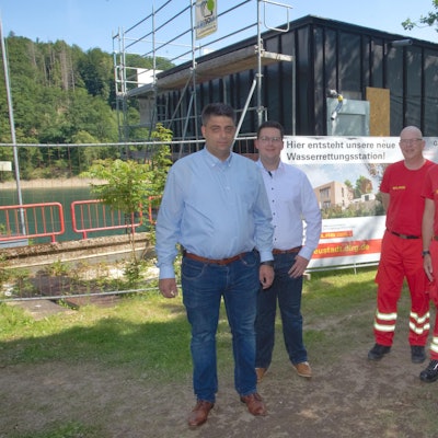 Vier Mitglieder der DLRG stehen an der Aggertalsperre vor einem Rohbau.