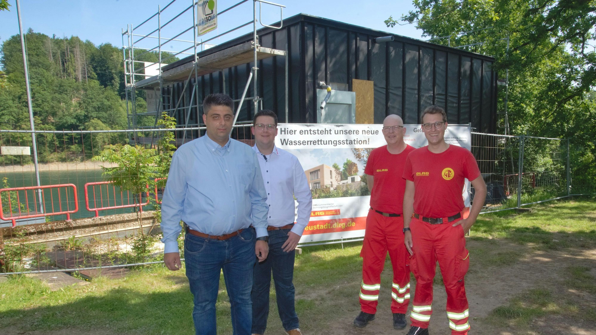 Vier Mitglieder der DLRG stehen an der Aggertalsperre vor einem Rohbau.