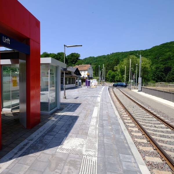Der Haltepunkt in Urft erstrahlt in neuem Glanz. Im Hintergrund passiert ein blaues Auto den Bahnübergang.