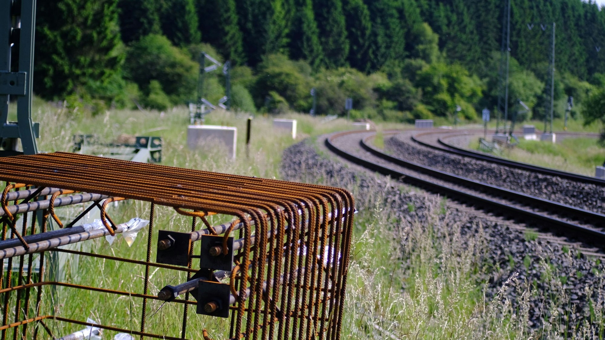 Entlang der Eifelstrecke im Urfttal zwischen Nettersheim und Blankenheim sind Mastfundamente zu sehen. Im Vordergrund liegt ein eiserner Bewährungskorb.