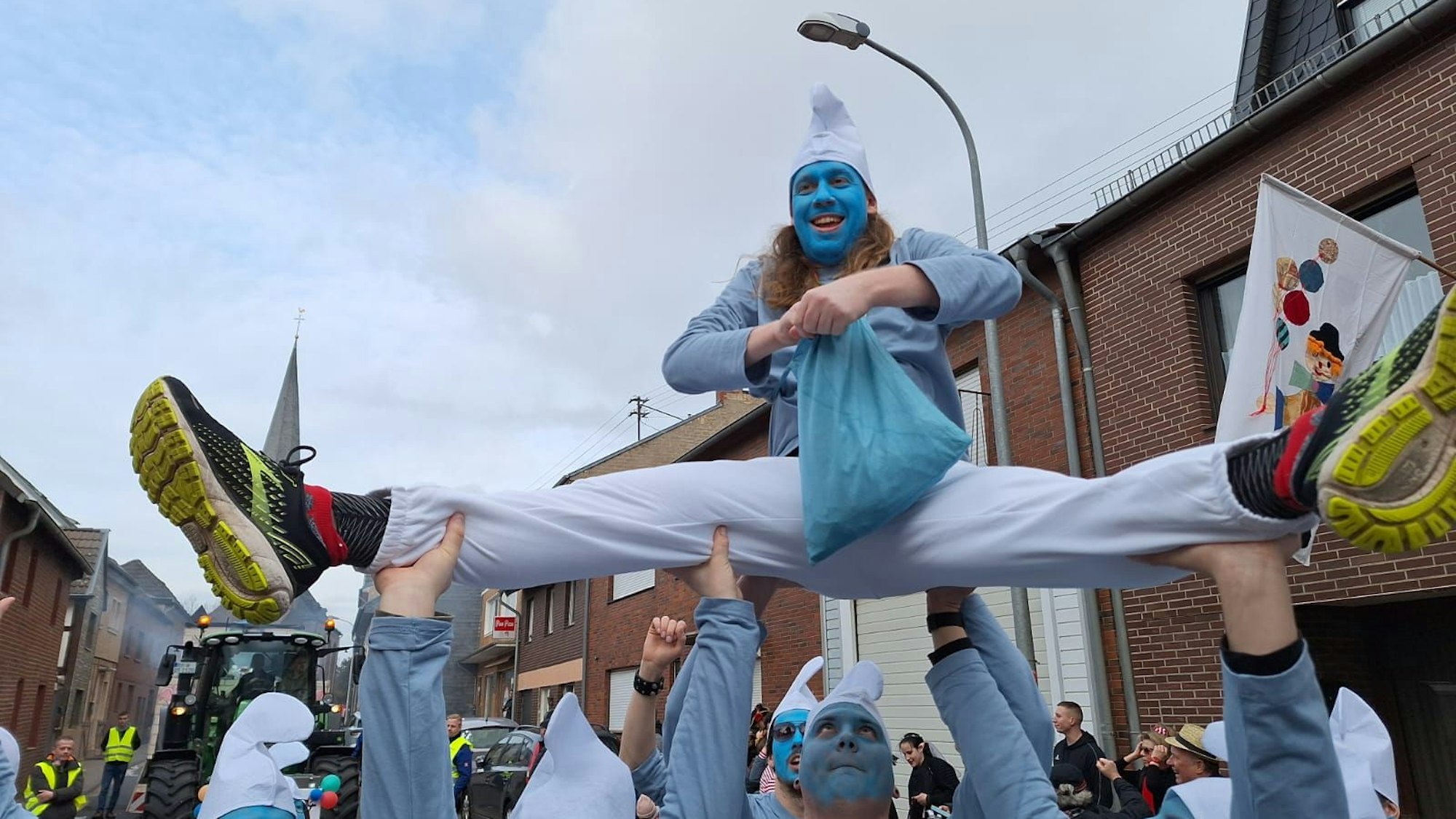 Philipp Tontsch macht als Schlumpf verkleidet einen Spagat, während er von anderen kostümierten Schlümpfen in die Luft gehoben wird.
