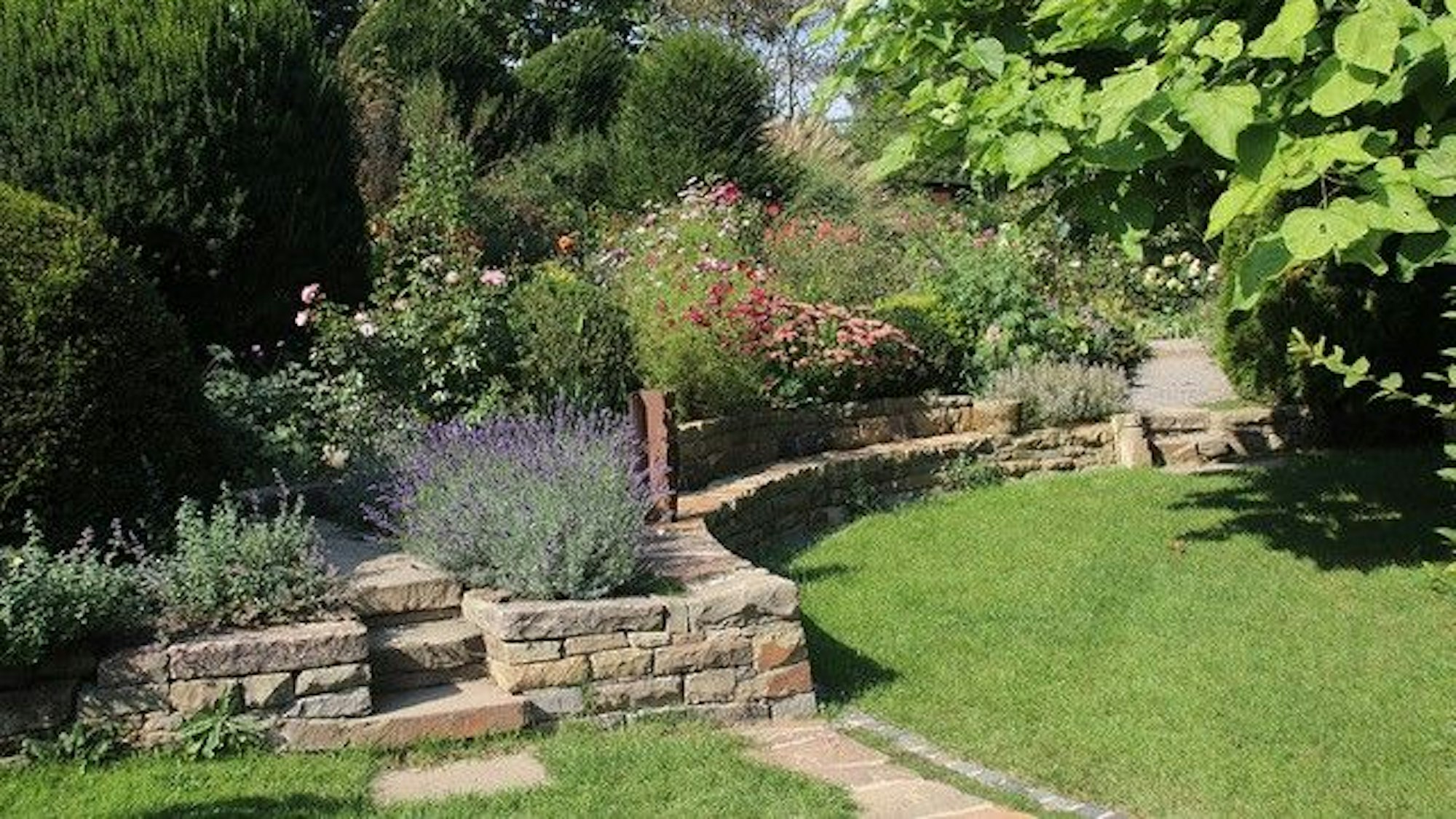 Ein Blumenbeet wird durch eine Mauer vom Rasen abgetrennt.