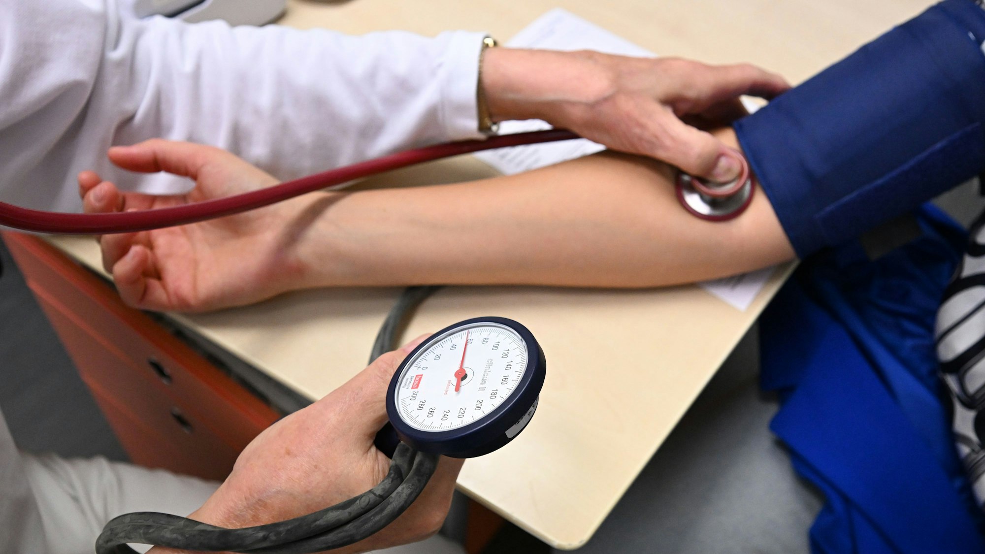 Ein Arzt misst in einer Bereitschaftspraxis in einem Krankenhaus in einem Untersuchungsraum bei einer Patientin den Blutdruck.