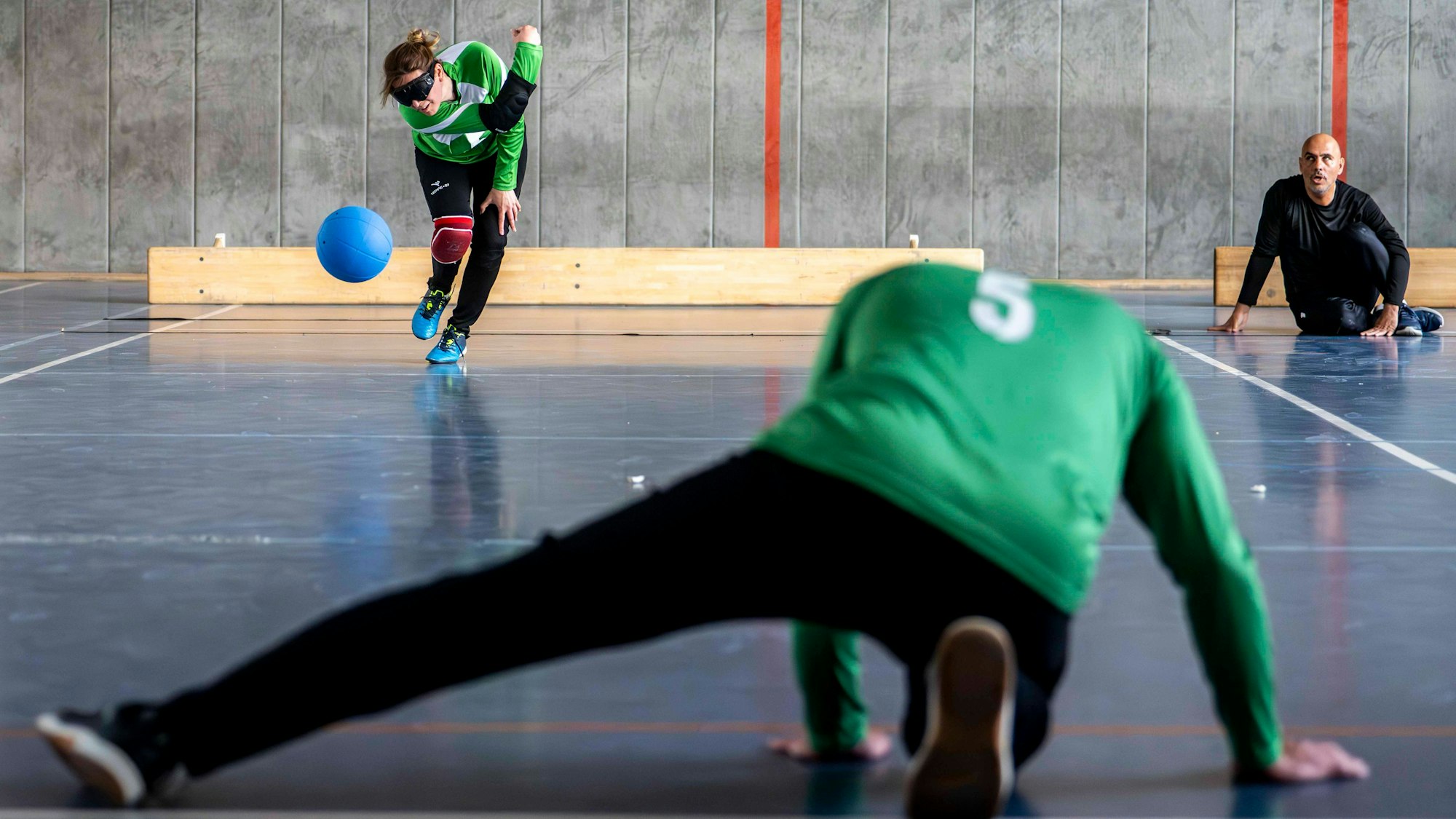 Das Bild zeigt eine Szene beim Goalball. Der Ball wird wie beim Kegeln in Richtung Gegner geworfen.
