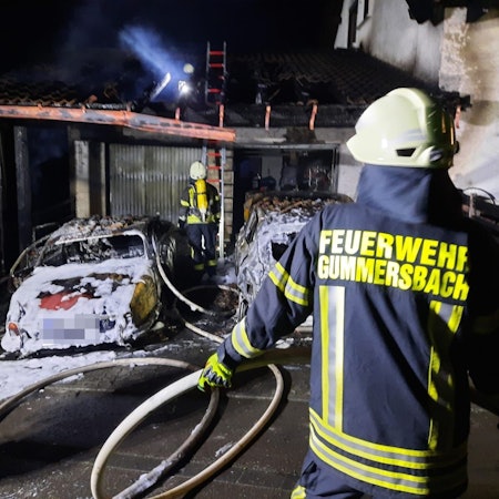 Ein Feuerwehrmann löscht zwei brennende Autos in einem Carport.