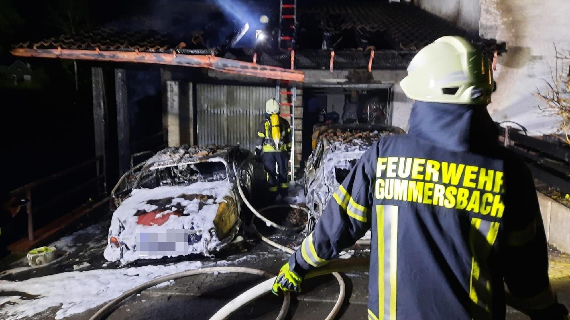 Ein Feuerwehrmann löscht zwei brennende Autos in einem Carport.