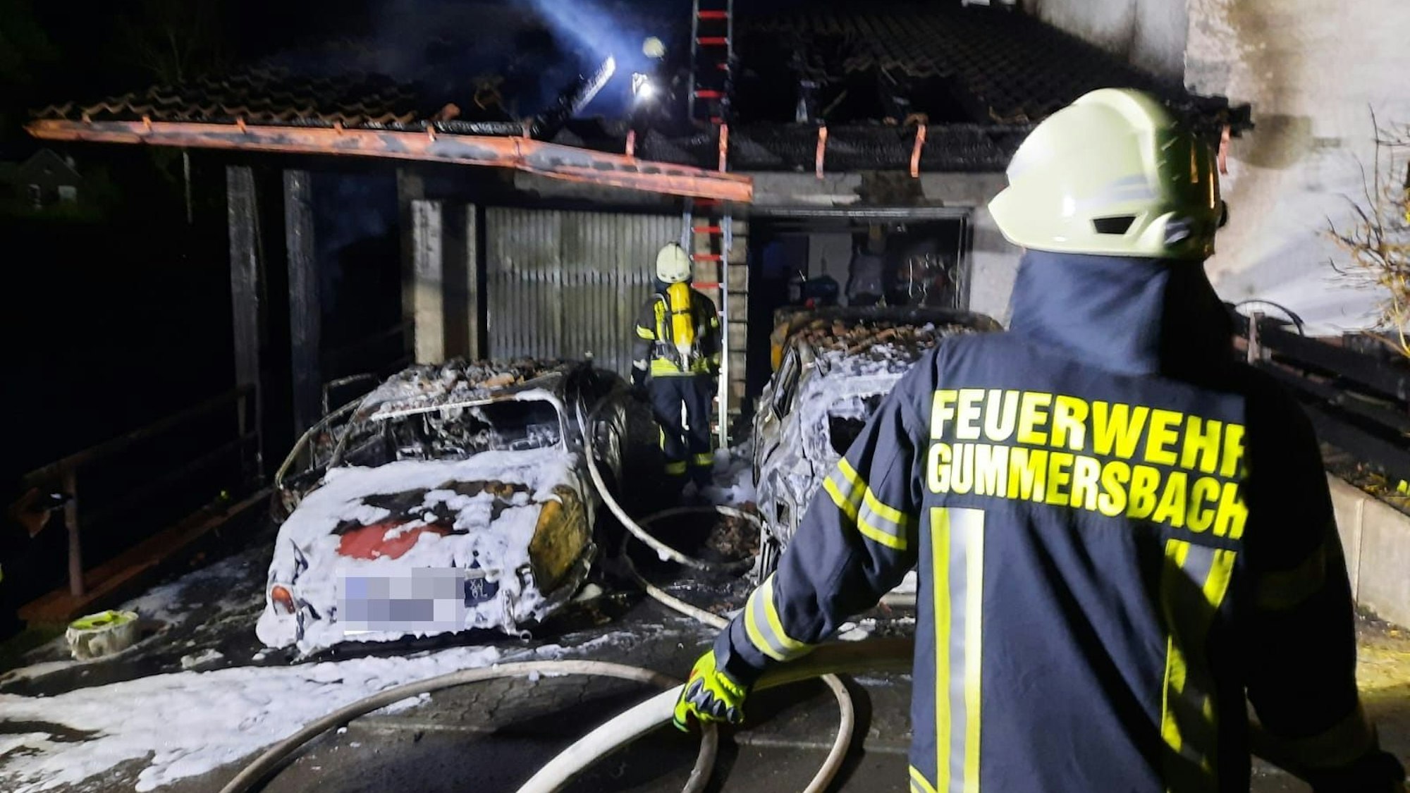 Ein Feuerwehrmann löscht zwei brennende Autos in einem Carport.
