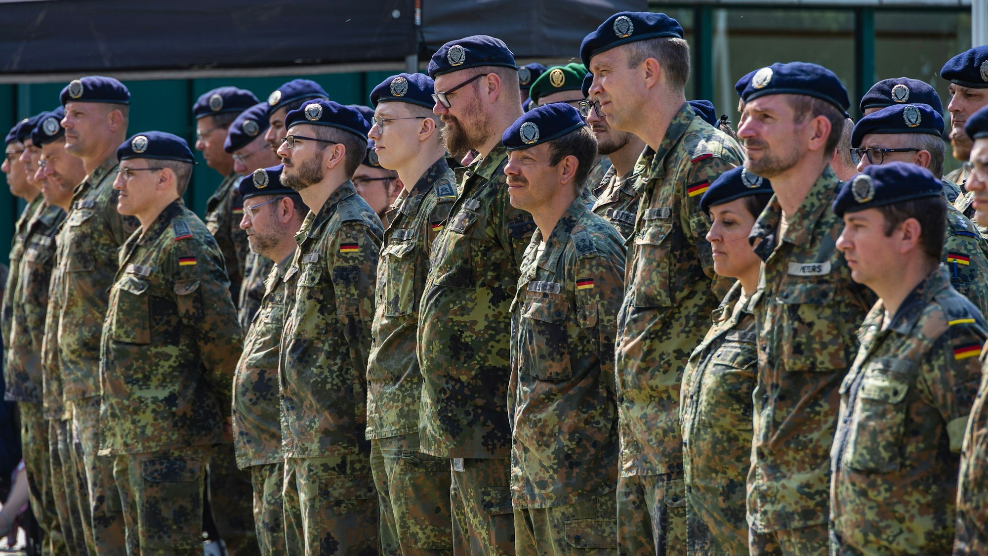 Die Soldatinnen und Soldaten stehen in Feldanzeigen mit blauen Baretts in Reih und Glied.