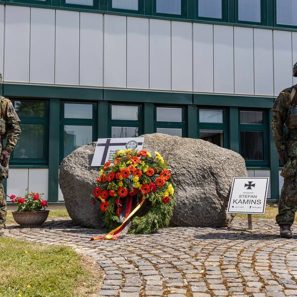 Zwei voll ausgerüstete Soldaten stehen neben einem Stein, an dem sie zuvor einen Kranz niedergelegt haben. Ein Schild weist auf den in Afghanistan gefallenen Stabsgefreiten Stefan Kamins hin.