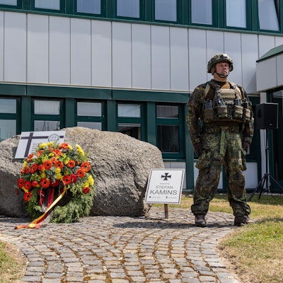 Zwei voll ausgerüstete Soldaten stehen neben einem Stein, an dem sie zuvor einen Kranz niedergelegt haben. Ein Schild weist auf den in Afghanistan gefallenen Stabsgefreiten Stefan Kamins hin.