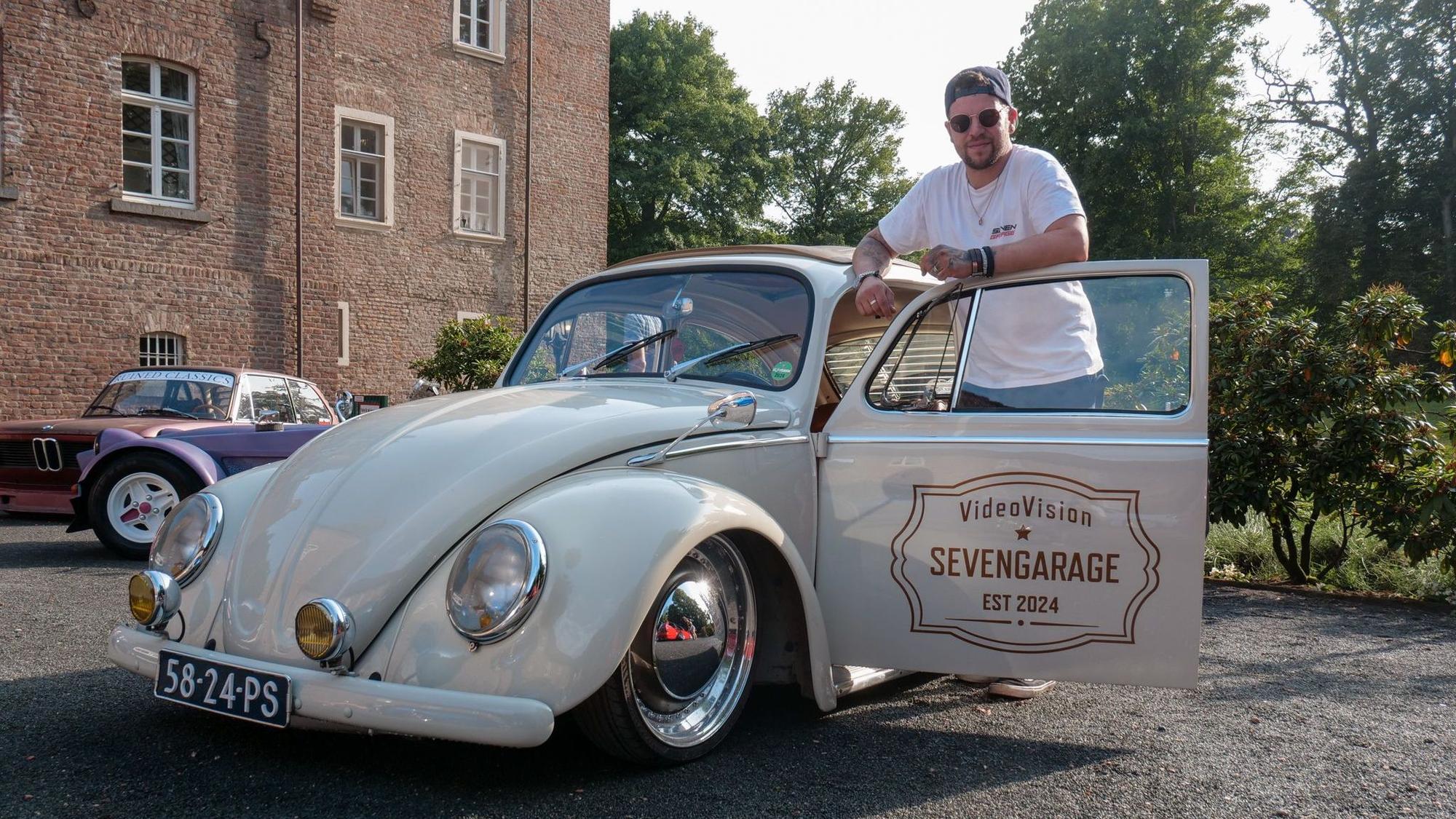 Das Foto zeigt einen Mann, der hinter der offenen Tür eines VW Käfers an seinem Wagen lehnt.