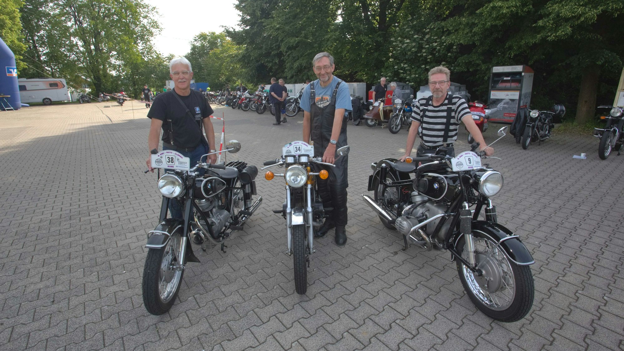 Drei Männer stehen mit ihren Motorrädern in einer Reihe.