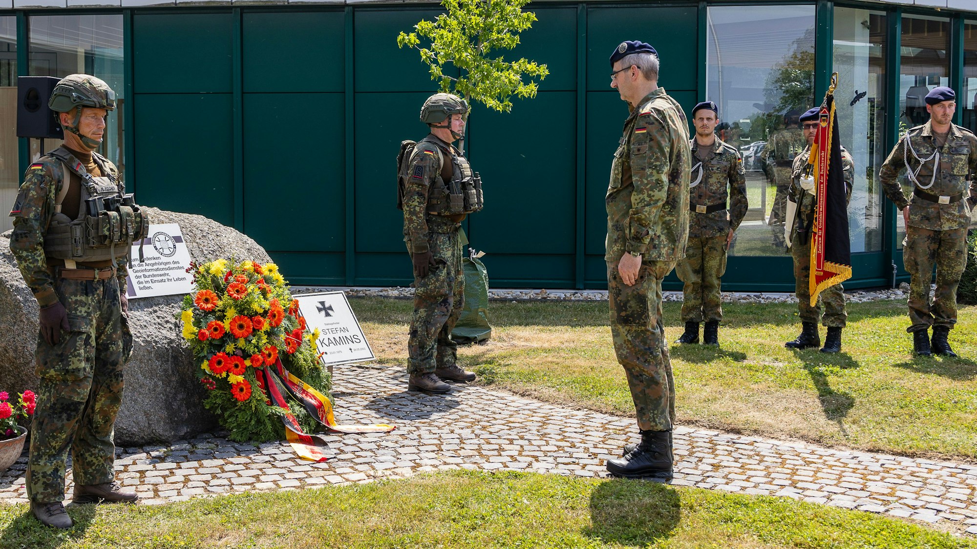 Der Brigadegeneral steht vor dem Stein, an dem die Soldaten den Kranz abgelegt haben. Im Hintergrund steht eine Ehrenwache mit gesenkter Fahne.